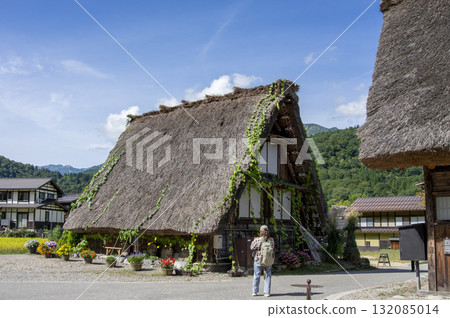 A person photographing the Gassho-zukuri style houses of Shirakawa-go, a World Heritage Site, and summer loofahs A person photographing the Gassho-zukuri style houses of Shirakawa-go, a World Heritage Site, and summer loofahs 132085014