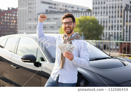 A man is holding cash and celebrating next to a black car, likely indicating financial success or a purchase. A man is holding cash and celebrating next to a black car, likely indicating financial success or a purchase. 132086459