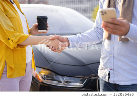 Two people shaking hands in front of a car, possibly after a business deal. 132086486
