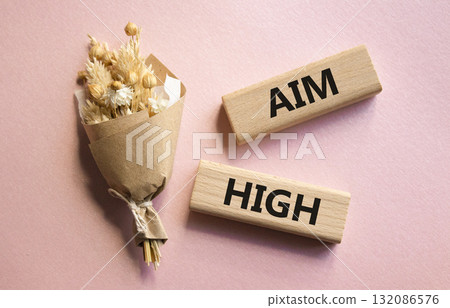 Aim High symbol. Wooden blocks with words Aim High. Beautiful pink background with bouquet of flowers. Business and Aim High concept. Copy space. Aim High symbol. Wooden blocks with words Aim High. Beautiful pink background with bouquet of flowers. Business and Aim High concept. Copy space. 132086576
