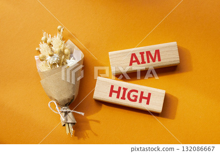 Aim High symbol. Wooden blocks with words Aim High. Beautiful orange background with bouquet of flowers. Business and Aim High concept. Copy space. 132086667