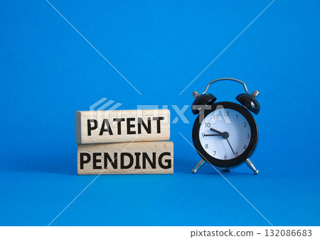 Patent Pending symbol. Wooden blocks with words Patent Pending. Beautiful blue background with alarm clock. Business and Patent Pending concept. Copy space. 132086683