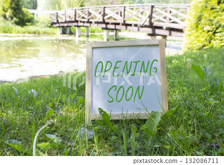 Opening soon symbol. Concept word Opening soon on white chalk blackboard. Beautiful meadow background with bridge. Business and Opening soon concept. Copy space. Opening soon symbol. Concept word Opening soon on white chalk blackboard. Beautiful meadow background with bridge. Business and Opening soon concept. Copy space. 132086711