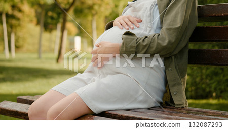 Woman carrying a baby sitting on a bench in the park. Woman carrying a baby sitting on a bench in the park. 132087293