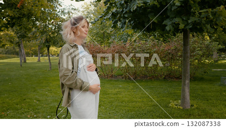 Woman with hands on belly walking outside in park living an active lifestyle during pregnancy 132087338