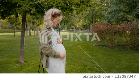 Walking pregnant female outside in park living an active lifestyle during pregnancy. Walking pregnant female outside in park living an active lifestyle during pregnancy. 132087347
