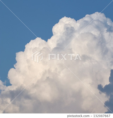 A majestic formation of towering, sunlit white cumulonimbus clouds against a deep blue sky, with dark grey shadows at the base, creating dramatic contrast and depth. A majestic formation of towering, sunlit white cumulonimbus clouds against a deep blue sky, with dark grey shadows at the base, creating dramatic contrast and depth. 132087667