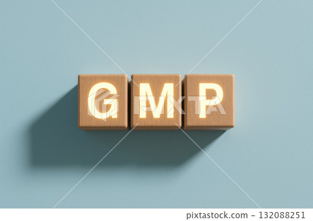 Wooden blocks with glowing letters spelling "GMP" create striking visual against blue pastel background, emphasizing pharmaceutical compliance in clean, minimal composition 132088251