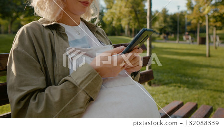 Shot of pregnant woman hands messaging while relaxing in nature. Shot of pregnant woman hands messaging while relaxing in nature. 132088339