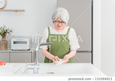 Senior / elderly woman washing dishes in the kitchen at home (smile) 132088821