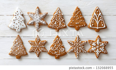 Assortment of Homemade Christmas Gingerbread Cookies: Overhead View of Festive Tree and Snowflake Shapes Decorated with White Icing and Powdered Sugar, Laid Out on White Wooden Table for the Holidays. Assortment of Homemade Christmas Gingerbread Cookies: Overhead View of Festive Tree and Snowflake Shapes Decorated with White Icing and Powdered Sugar, Laid Out on White Wooden Table for the Holidays. 132088955