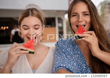 Watermelon Summer Friends Eating: Two young women joyfully enjoy watermelon slices outdoors on a sunny day, possibly at a cafe. Watermelon Summer Friends Eating: Two young women joyfully enjoy watermelon slices outdoors on a sunny day, possibly at a cafe. 132089567