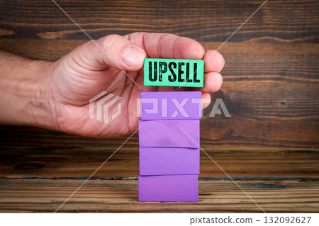 Hand holding green block with text UPSELL above stack of purple wooden blocks. Business growth 132092627