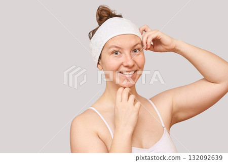 Young caucasian female smiling, wearing headband, light background, skincare Young caucasian female smiling, wearing headband, light background, skincare 132092639