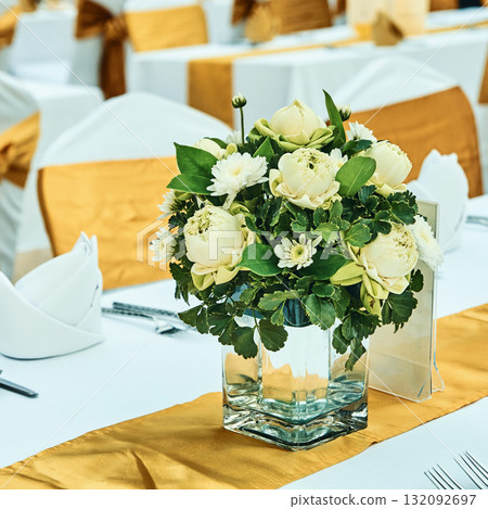 Elegant floral centerpiece with white roses on table with gold accents Elegant floral centerpiece with white roses on table with gold accents 132092697