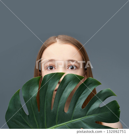 Young caucasian female with monstera leaf against gray background featuring Young caucasian female with monstera leaf against gray background featuring 132092751