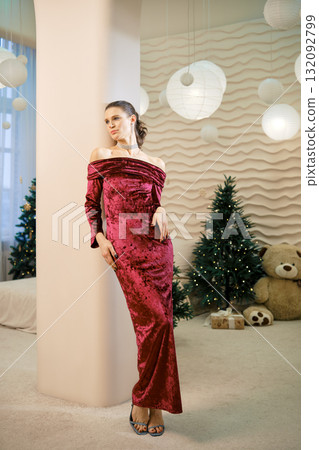 Elegant woman in red dress poses by Christmas decorations in cozy indoor setting 132092799