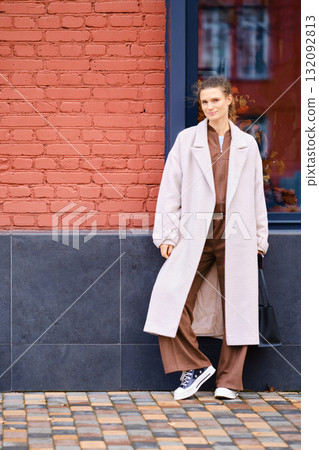 Stylish young woman poses against a red brick wall in an urban setting during daylight 132092813