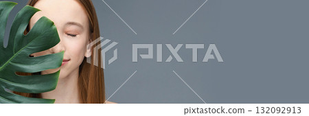 Young caucasian female with closed eyes posing behind large green leaf against 132092913