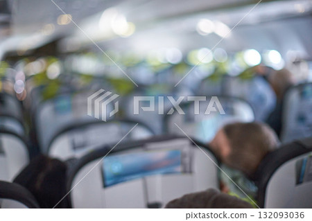 Blurry airplane interior with rows of seats and passengers in focus 132093036