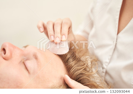 Female caucasian young adult receiving relaxing gua sha facial massage Female caucasian young adult receiving relaxing gua sha facial massage 132093044