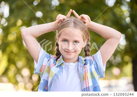 Caucasian young girl smiling outdoors with pigtails and playful gesture 132093244