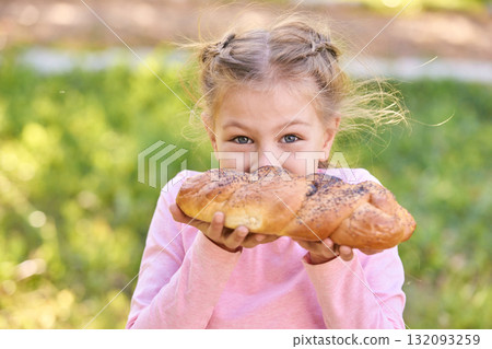 Caucasian blonde young girl enjoying fresh baked bread outdoors, smiling Caucasian blonde young girl enjoying fresh baked bread outdoors, smiling 132093259