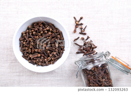 Dried cloves, in a white bowl, on linen. Aromatic flower buds of the tree Syzygium aromaticum, used as spice, fragrance, and for flavoring in cuisine and cosmetic products. Close-up, from above. Photo Dried cloves, in a white bowl, on linen. Aromatic flower buds of the tree Syzygium aromaticum, used as spice, fragrance, and for flavoring in cuisine and cosmetic products. Close-up, from above. Photo 132093263