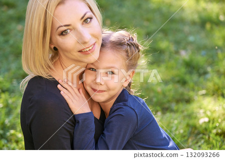 Caucasian female adult hugging young child in green park, both smiling, bonding Caucasian female adult hugging young child in green park, both smiling, bonding 132093266