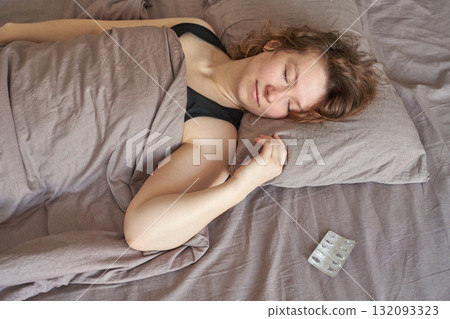 Young caucasian female sleeping peacefully in bed with an empty medicine blister 132093323