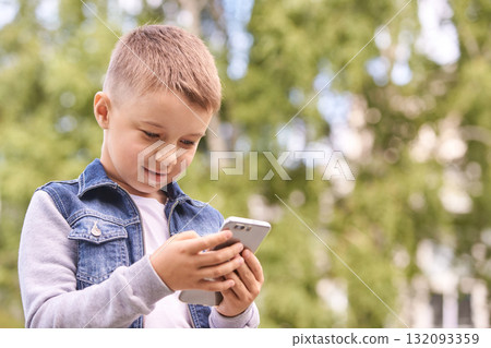 Smiling caucasian young boy with phone in outdoor park on a sunny day 132093359