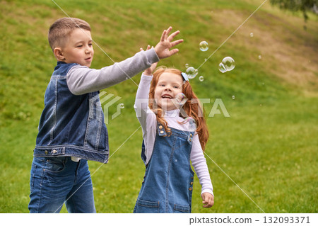 Caucasian children enjoying bubbles outdoors with smiling faces in a green park 132093371