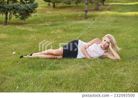Caucasian young female lying on grass in park wearing white top and black skirt Caucasian young female lying on grass in park wearing white top and black skirt 132093500