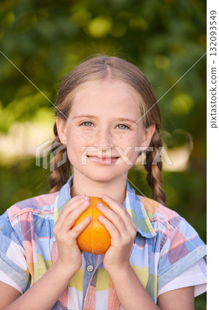 Caucasian young girl holding orange with braided hair in colorful shirt Caucasian young girl holding orange with braided hair in colorful shirt 132093549