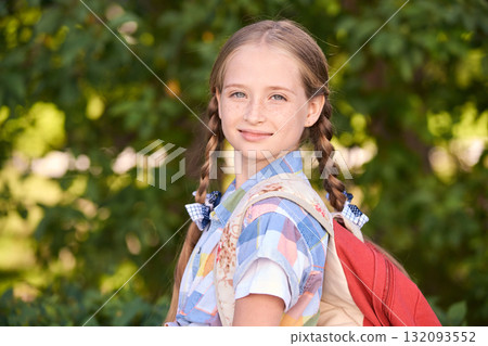 Smiling young caucasian girl with pigtails and backpack enjoying nature Smiling young caucasian girl with pigtails and backpack enjoying nature 132093552