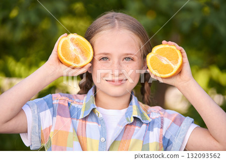 Smiling caucasian female child holding orange halves outdoors in plaid shirt 132093562