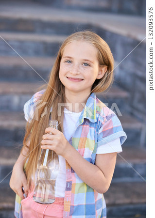 Smiling caucasian young girl holding bottle on stone steps outdoors in casual Smiling caucasian young girl holding bottle on stone steps outdoors in casual 132093576