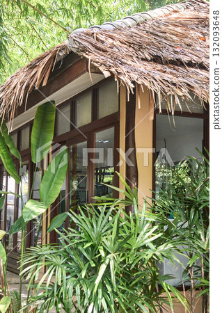 Tropical hut with palm fronds and lush greenery in a serene garden setting 132093648