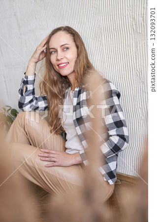 Caucasian young adult female in checkered shirt sitting indoors with natural Caucasian young adult female in checkered shirt sitting indoors with natural 132093701