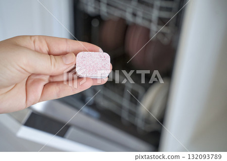 Hand holding dishwasher tablet in kitchen with open dishwasher in background Hand holding dishwasher tablet in kitchen with open dishwasher in background 132093789