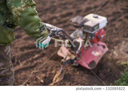 Adult male using tiller in field wearing camouflage clothing for farming Adult male using tiller in field wearing camouflage clothing for farming 132093822