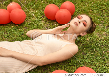 Young caucasian female relaxing with red balloons on grass in summer daydream Young caucasian female relaxing with red balloons on grass in summer daydream 132093830