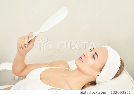 Young caucasian female relaxing in spa, holding hand mirror, wearing headband Young caucasian female relaxing in spa, holding hand mirror, wearing headband 132093831