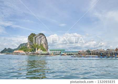 Scenic coastal village with rocky cliffs and blue sky reflections on calm water 132093835