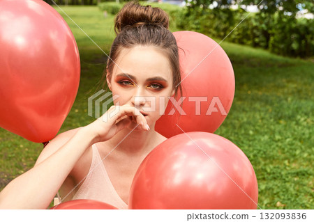 Young caucasian female surrounded by red balloons in a green park setting Young caucasian female surrounded by red balloons in a green park setting 132093836