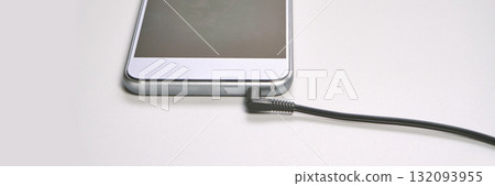 Smartphone with headphone jack connected via cable on white surface 132093955