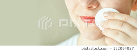 Caucasian female using cotton pad to remove lipstick from face close-up 132094087