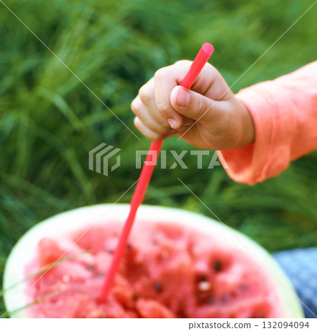 Childs hand holding straw in watermelon outdoors on grass background 132094094