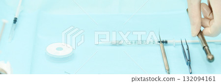 Surgical tools and medical equipment on blue surface with gloved hand preparing 132094161