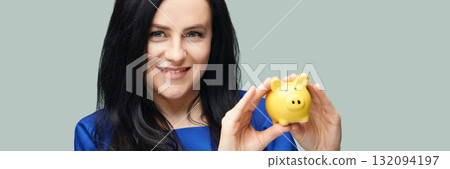 Caucasian female adult holding yellow piggy bank smiling in blue outfit against Caucasian female adult holding yellow piggy bank smiling in blue outfit against 132094197